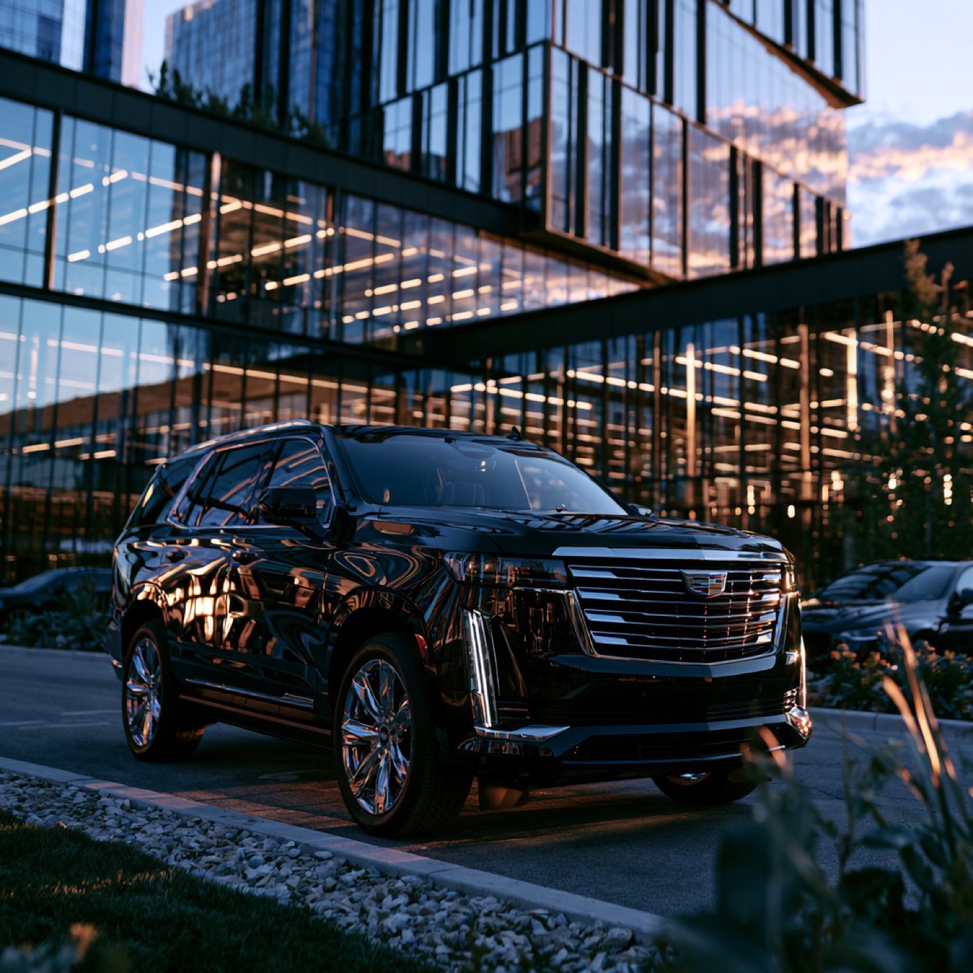 Black Cadillac Escalade parked outside a modern glass office building at dusk