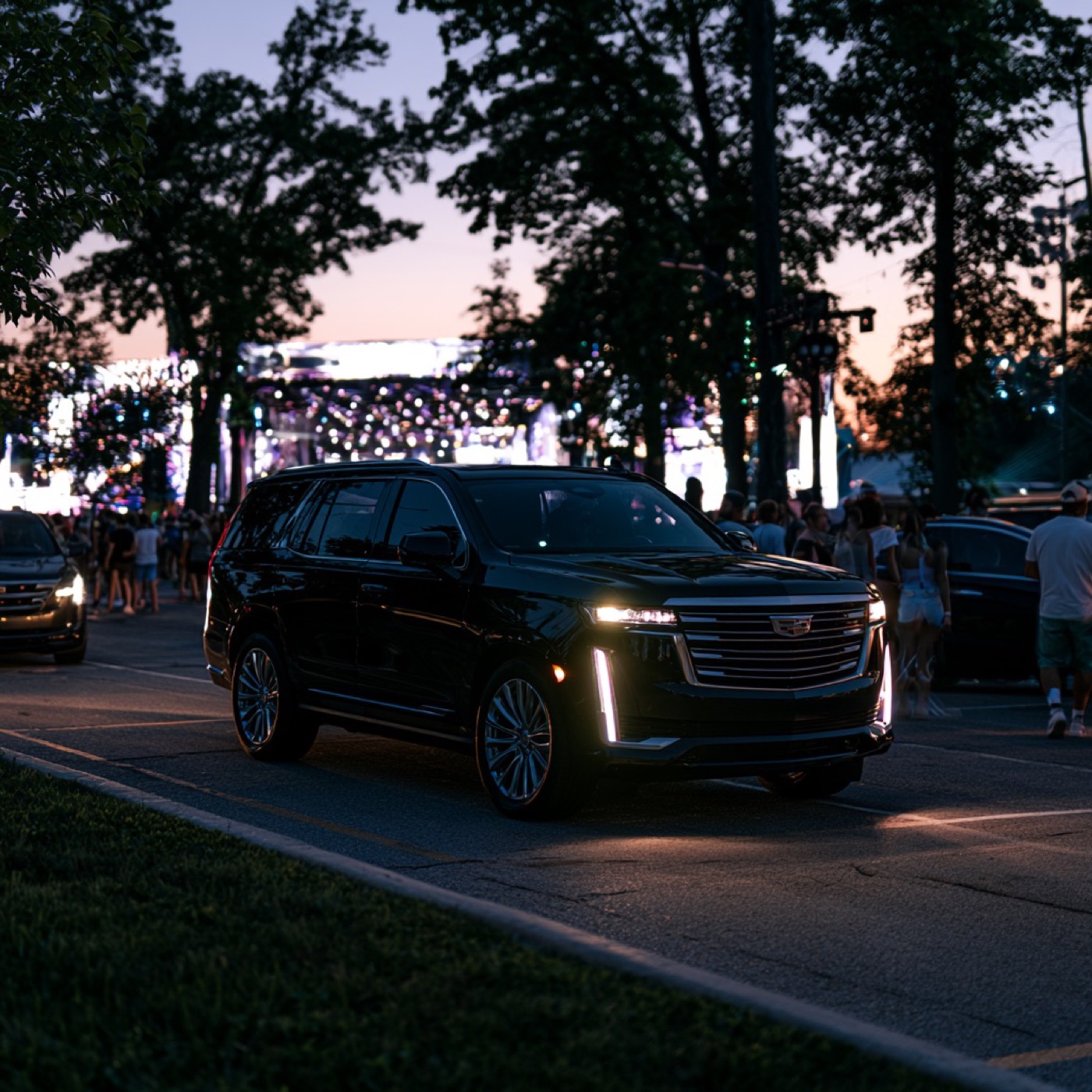 Black Cadillac Escalade arriving at a lively waterfront event at dusk